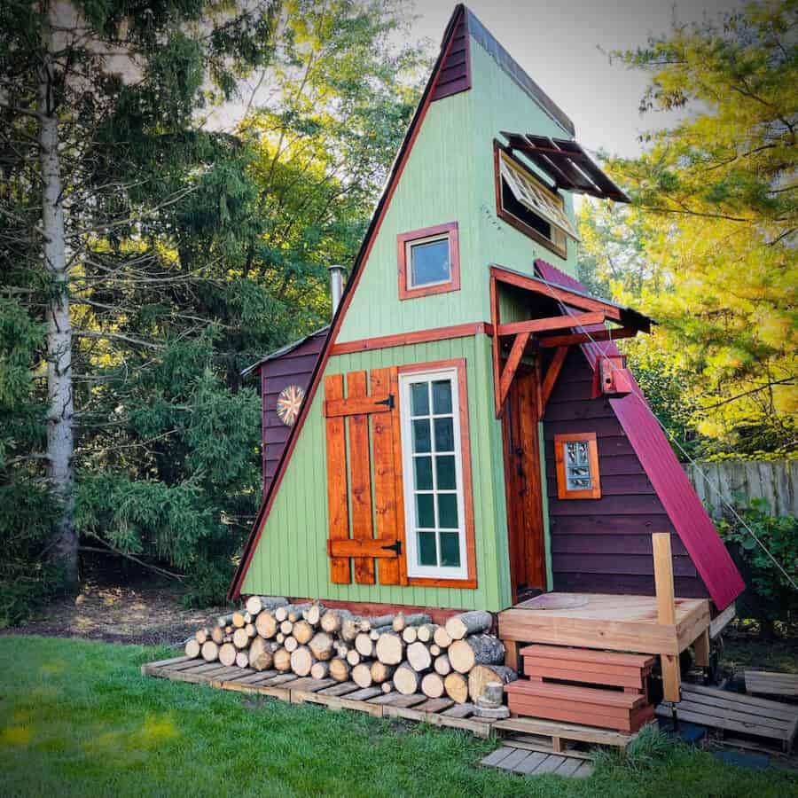 Colorful off-grid tiny cabin with vibrant green, purple, and red accents in a wooded setting.