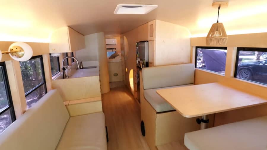 Interior of a compact tiny house with light wood finishes and large windows.