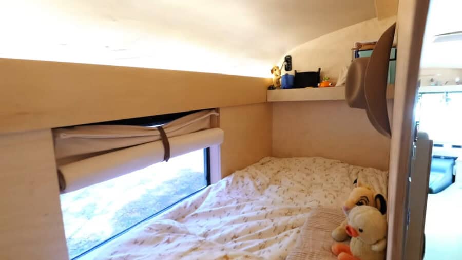 Interior view of a tiny house bedroom with a large window and cozy bed with plush toys.