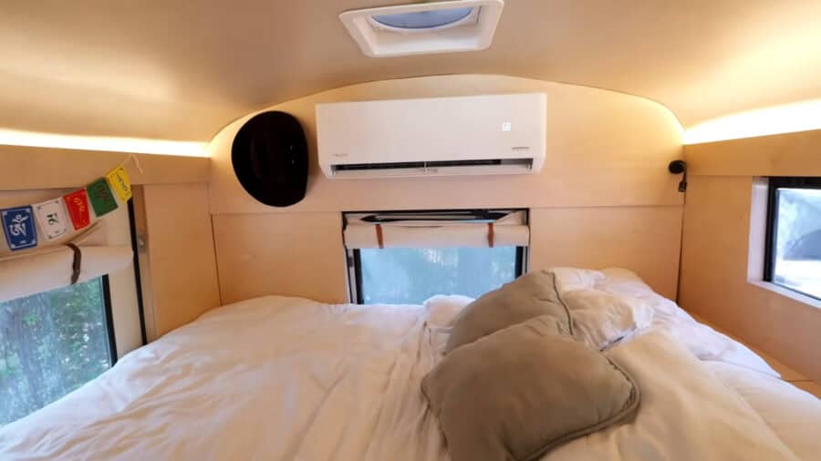 Compact tiny house bedroom with large windows and air conditioning.
