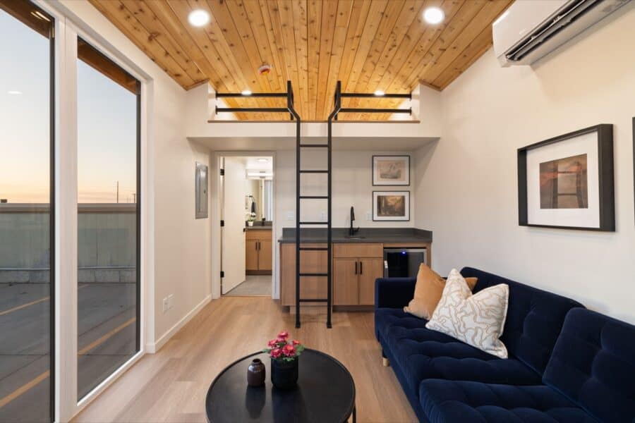 Cozy tiny house interior featuring a loft bed, modern furnishings, and large windows for natural lig.