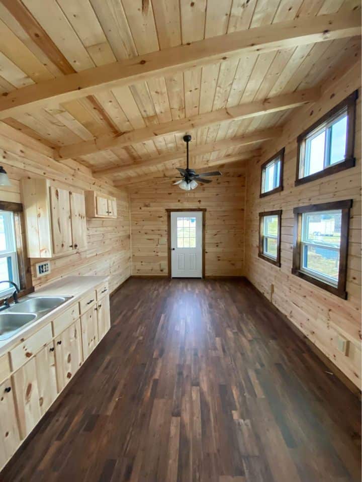 Cozy tiny house interior featuring natural wood walls, multiple windows, and a ceiling fan, perfect.