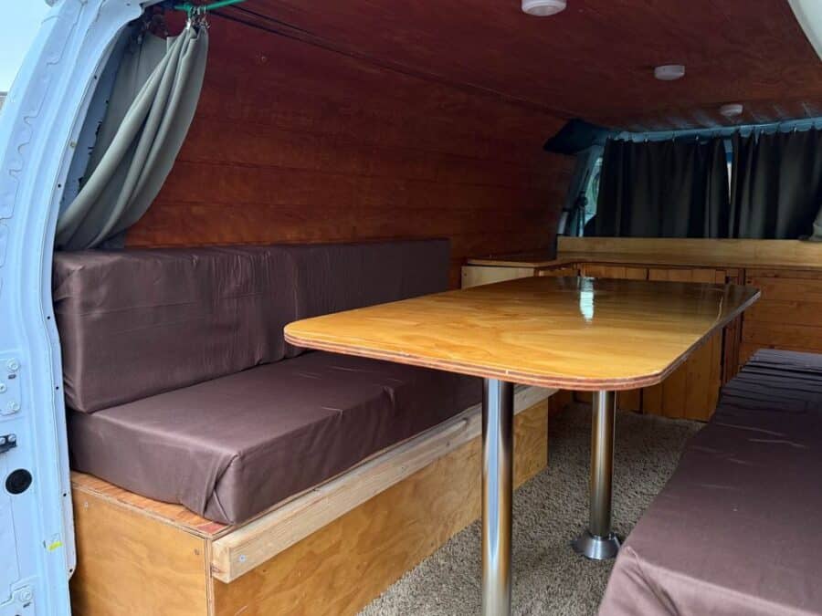 Interior of a Ford E150 campervan with cozy seating and wooden accents.