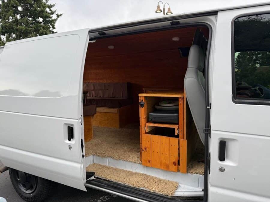 Interior view of a Ford E150 campervan with wooden furniture and cozy living space.