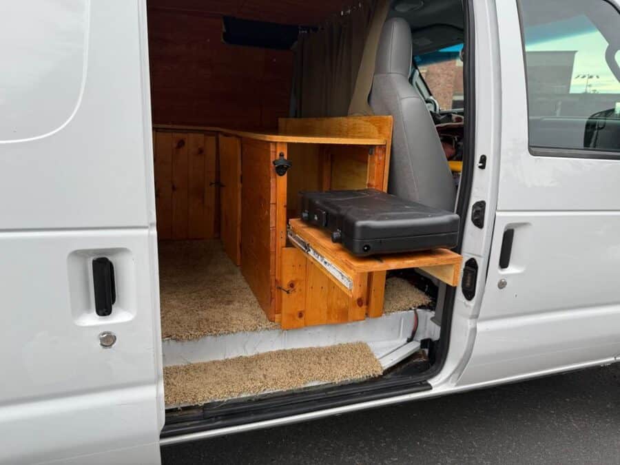 Ford E150 campervan interior with custom wood desk and seating for small space living.