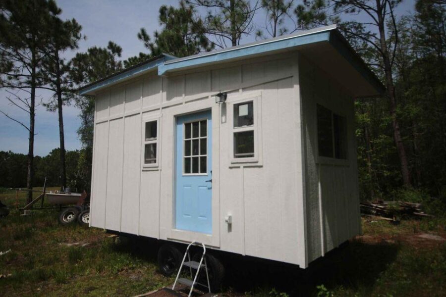 Tiny house with white exterior and blue door in Houston, perfect for small space living.