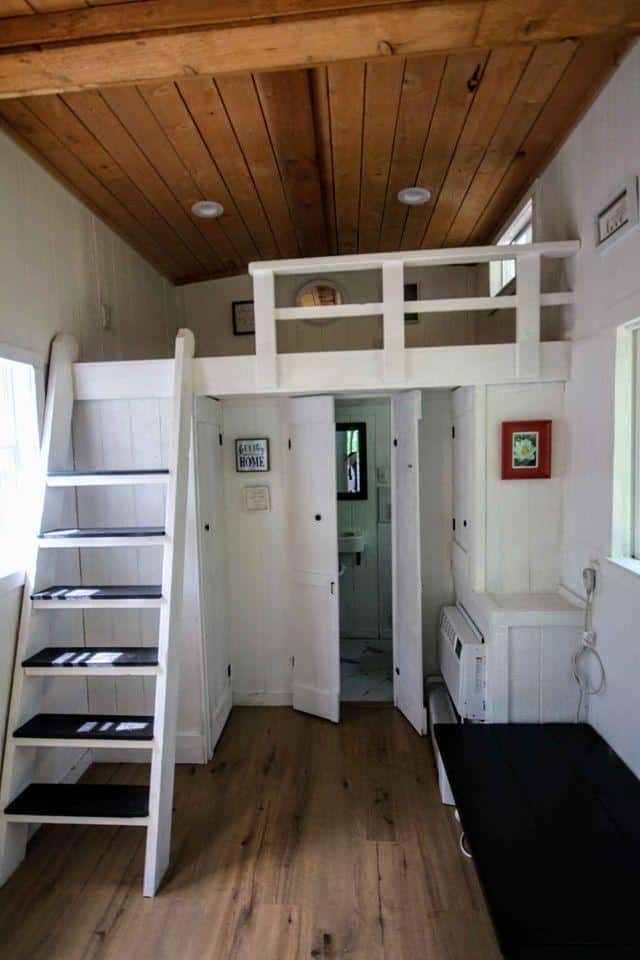 Cozy tiny house interior with loft, white wood walls, and wooden ceiling.