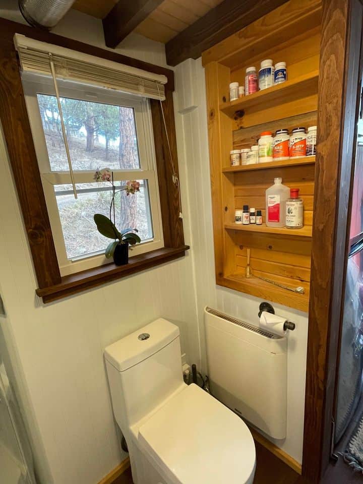 Compact tiny house bathroom with wooden shelves and a modern toilet.