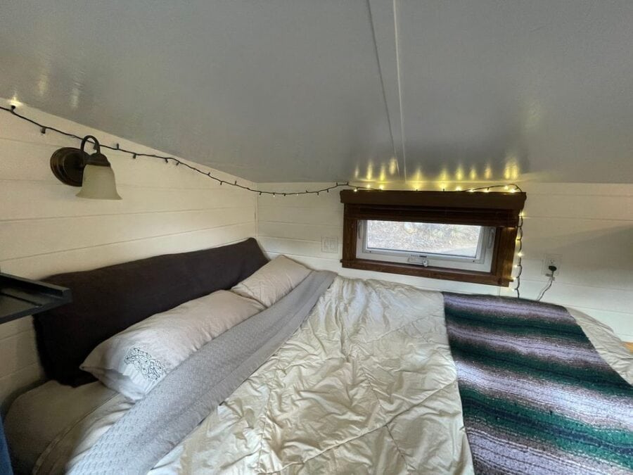 Tiny House Interior with cozy bed, string lights, and small window in a compact space.