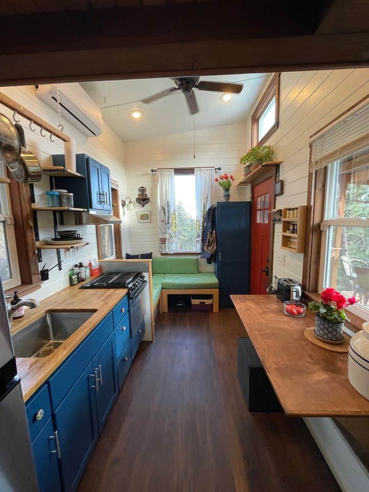Charming tiny house interior with blue cabinetry, a small kitchen, and a cozy seating nook by the wi.