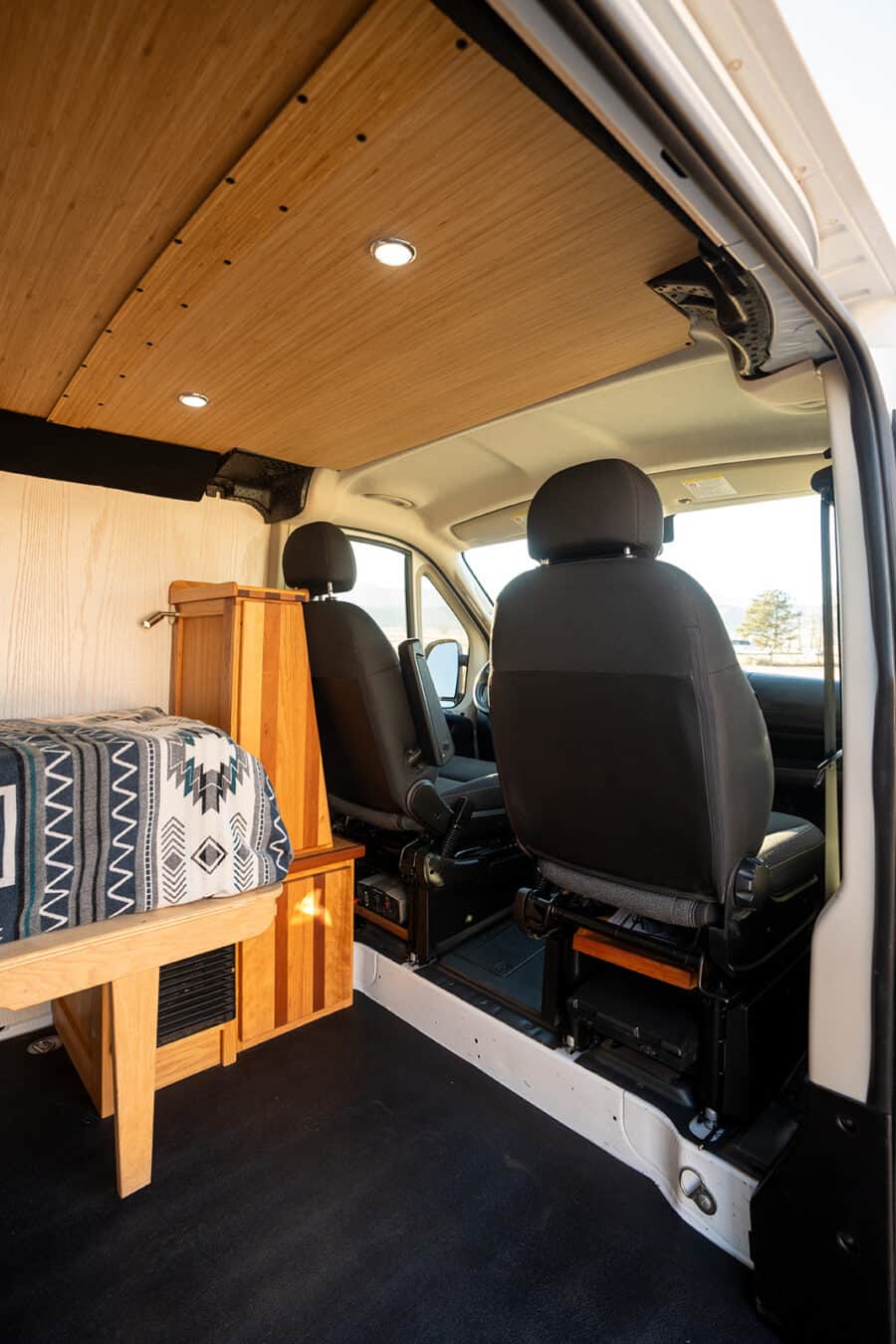 Interior view of a camper van showcasing wooden ceiling panels and cozy seating arrangement for trav.
