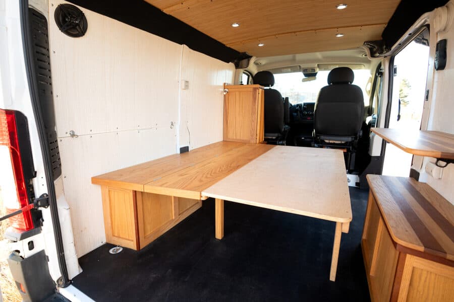 Interior of a Ram Promaster camper van featuring wooden fold-out table and storage solutions for sma.