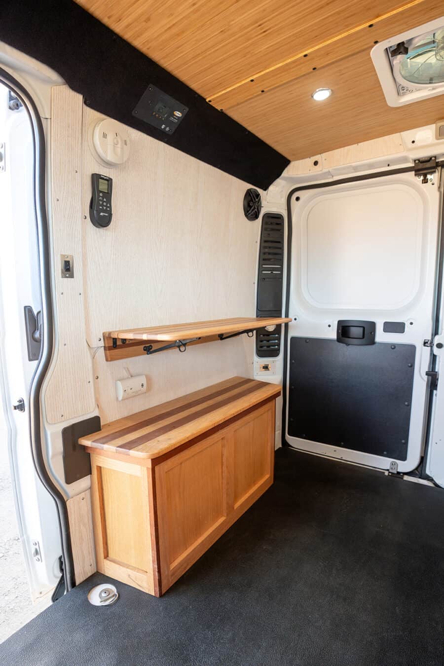 Efficient van conversion with wooden storage and workspace for travel adventures.