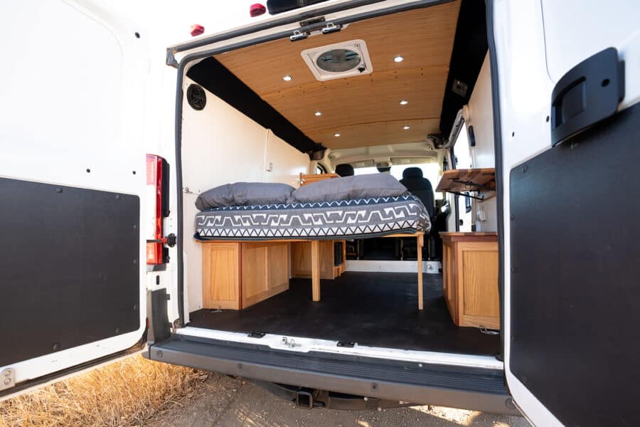 Interior view of a Ram Promaster camper van showcasing a cozy sleeping space with wooden cabinetry a.