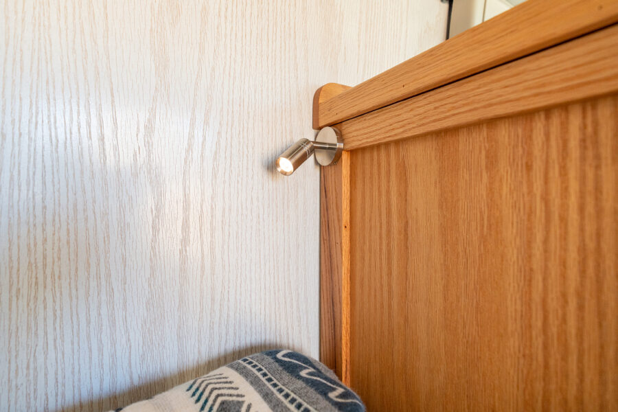 Wooden bed frame with built-in reading light in a cozy tiny house interior.