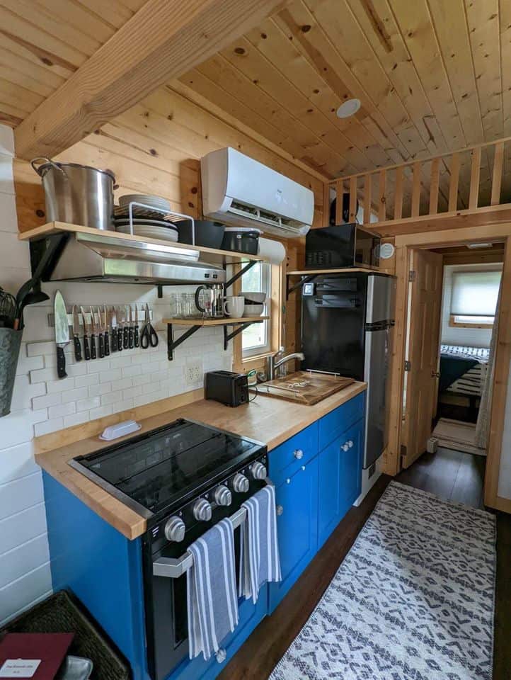 Compact tiny house kitchen with blue cabinets and wooden accents.