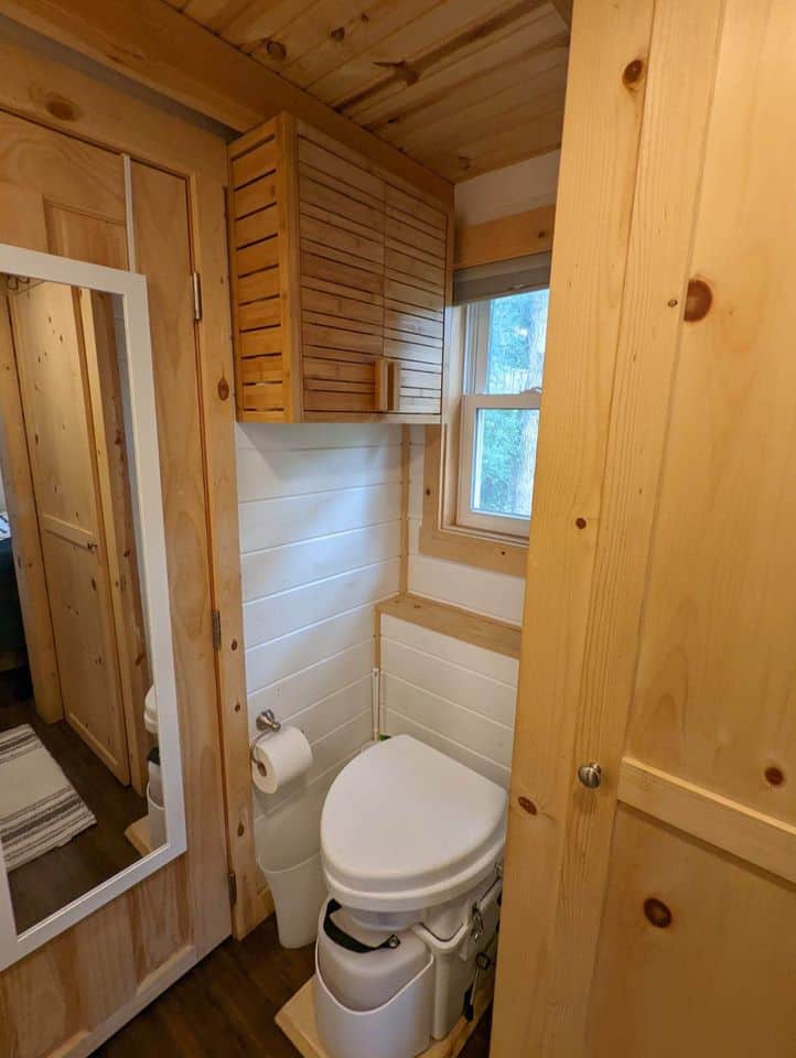 Interior view of a tiny house bathroom with wooden walls and a first-floor bedroom window.
