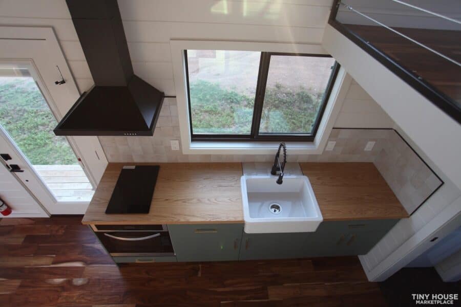 Modern tiny house kitchen with large window, farmhouse sink, and sleek cabinetry.