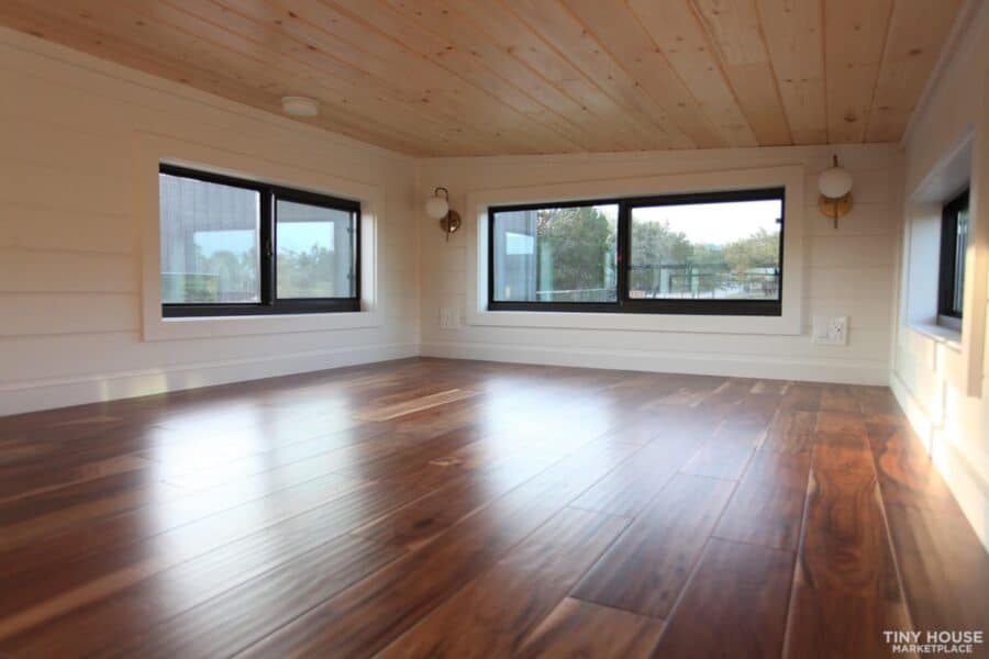 Bright interior of a 28′ NOAH-Certified tiny home with large windows and wooden floors.