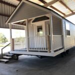 Family park model tiny home with porch and stairs, ideal for compact living and outdoor relaxation.