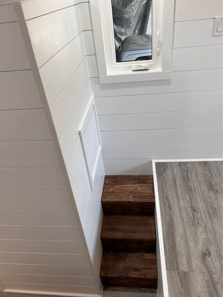 Compact tiny house interior featuring dark wood stairs and white shiplap walls.