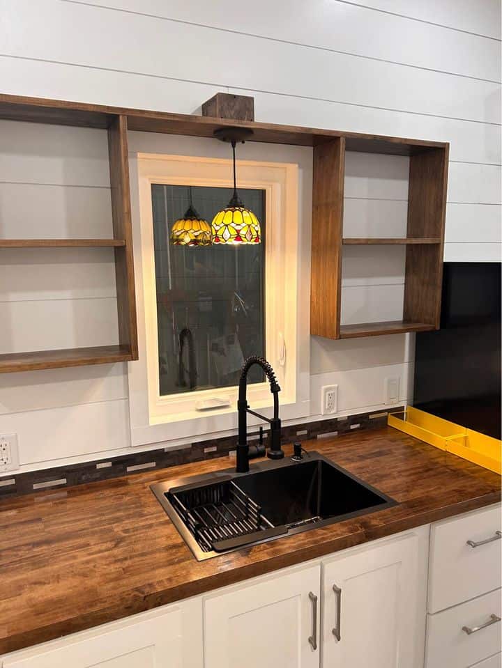 Compact kitchen featuring open wooden shelves and a black sink with a modern faucet.