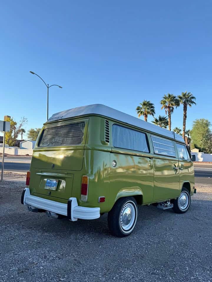 Sage green 1976 VW Westfalia camper bus with a white roof and whitewall tires, parked under palm trees