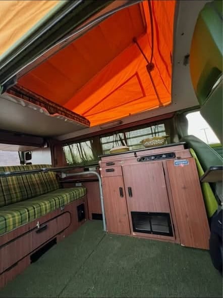 Interior with the pop-top raised, plaid bench seat, and wood cabinetry