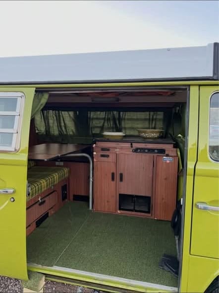 Open sliding door showing green carpet, plaid bench, and wood Westfalia cabinets