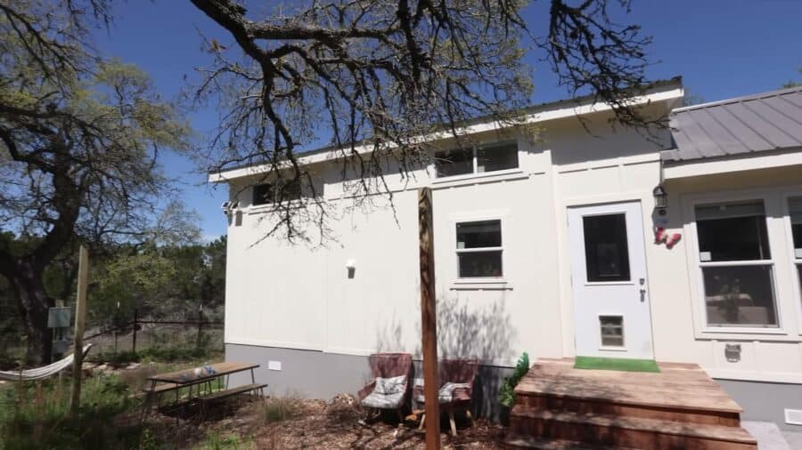 Back of a white tiny house with a wood deck and a door with a built-in dog door