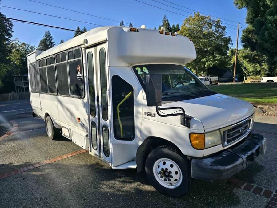 White 2004 Ford E450 shuttle bus with an Eldorado body parked in a driveway, seen from the front corner
