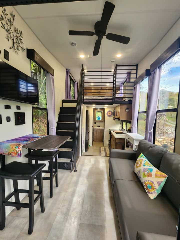 Living area with a black sofa, bar-height table, ceiling fan, and the metal stair to the front loft