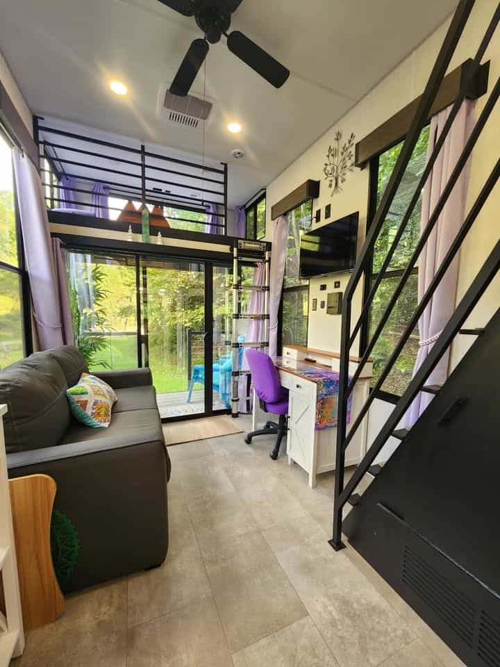 View toward the sliding glass door with a desk, sofa, and loft railing above