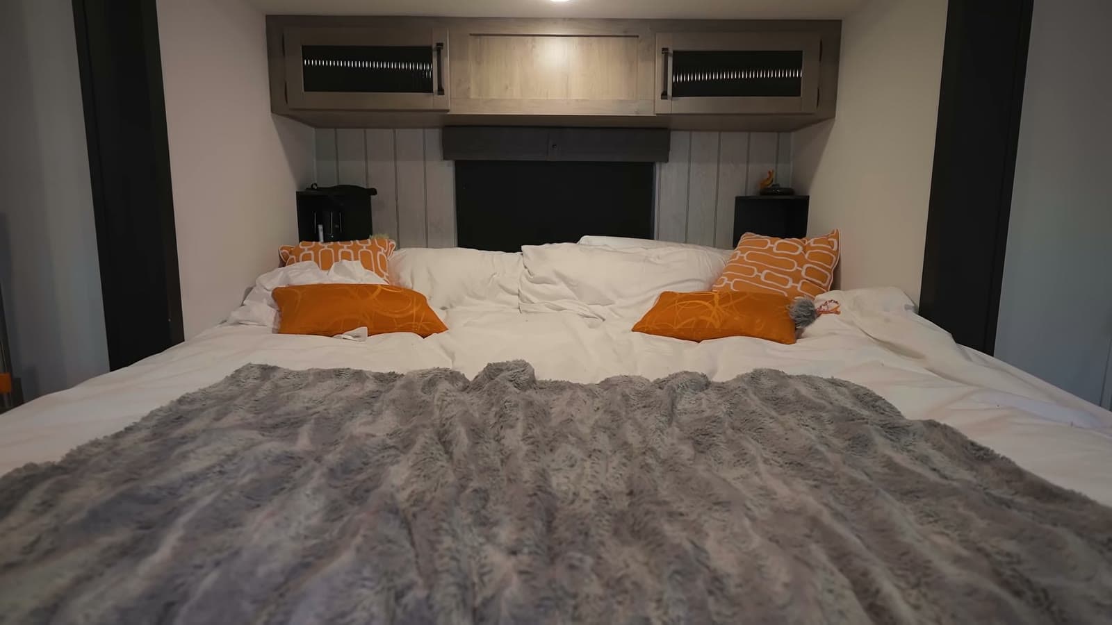 Main-floor bedroom with a king bed, gray throw, orange pillows, and overhead cabinets