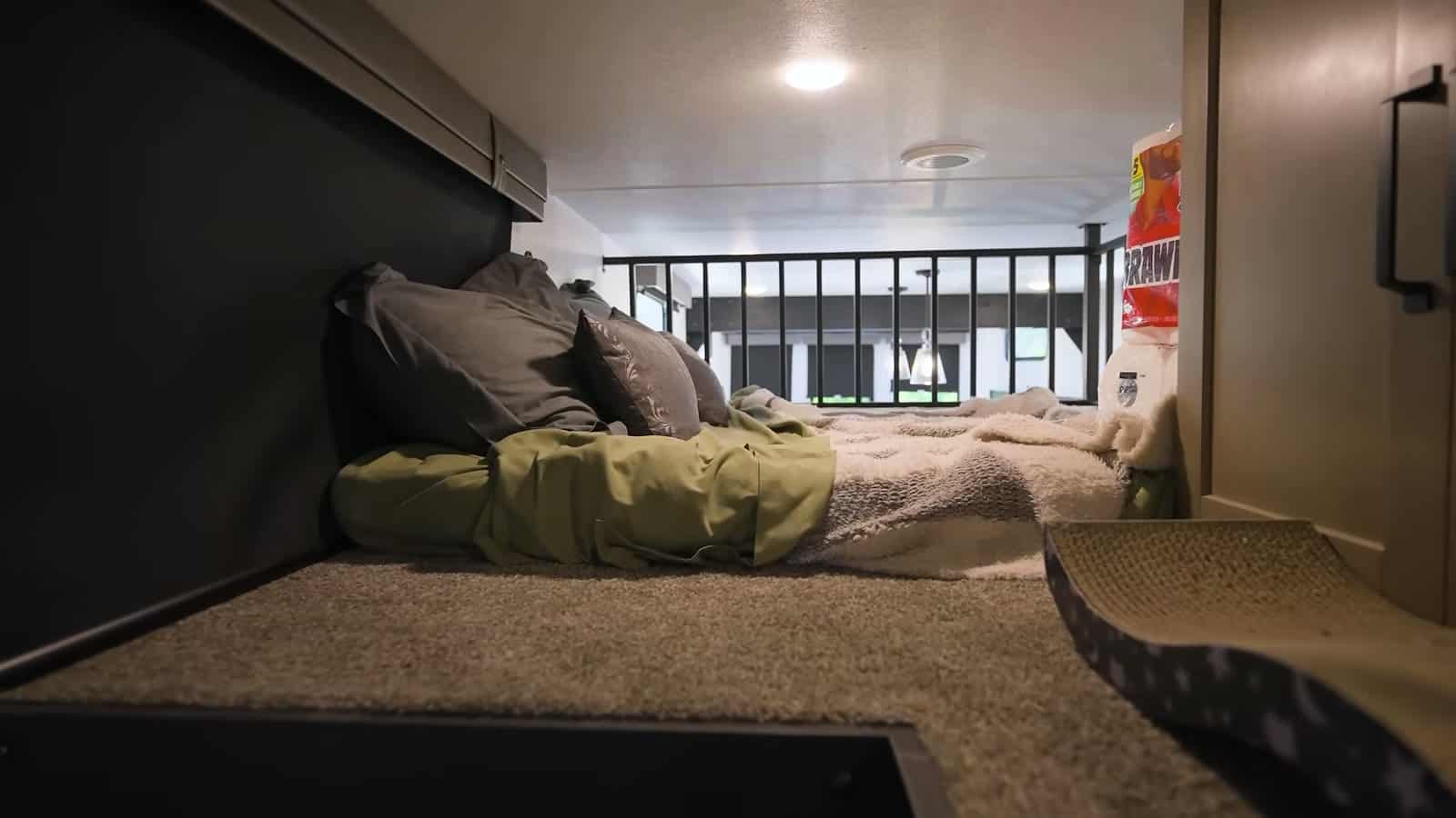 Carpeted loft above the bedroom with bedding and a railing overlooking the living area