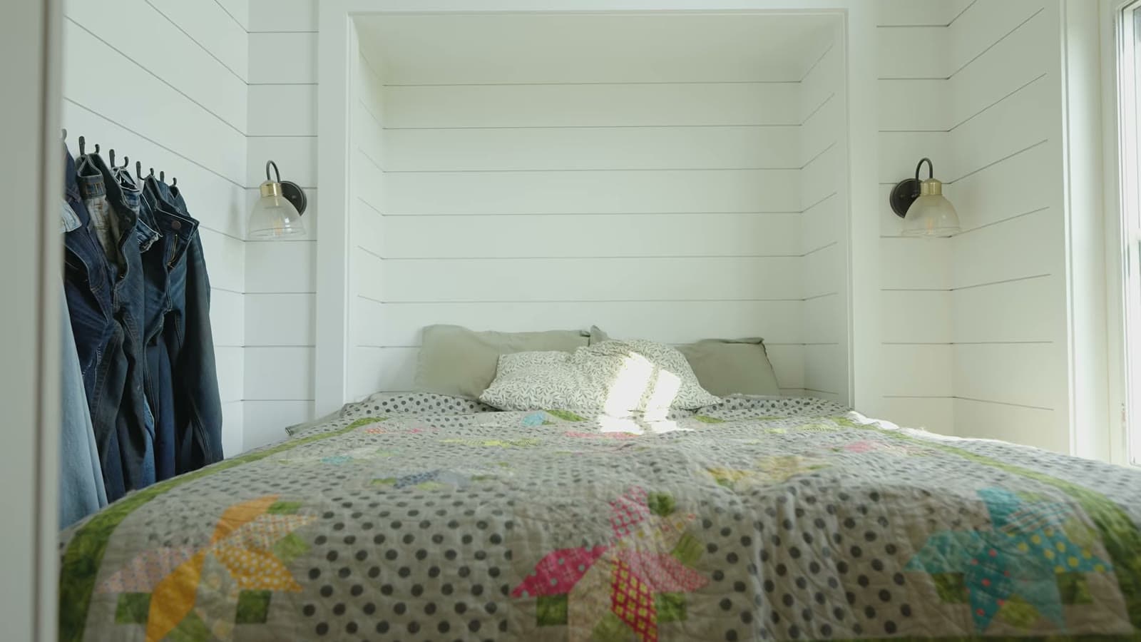Bedroom with white shiplap walls, two wall sconces, and a colorful patchwork quilt on the bed