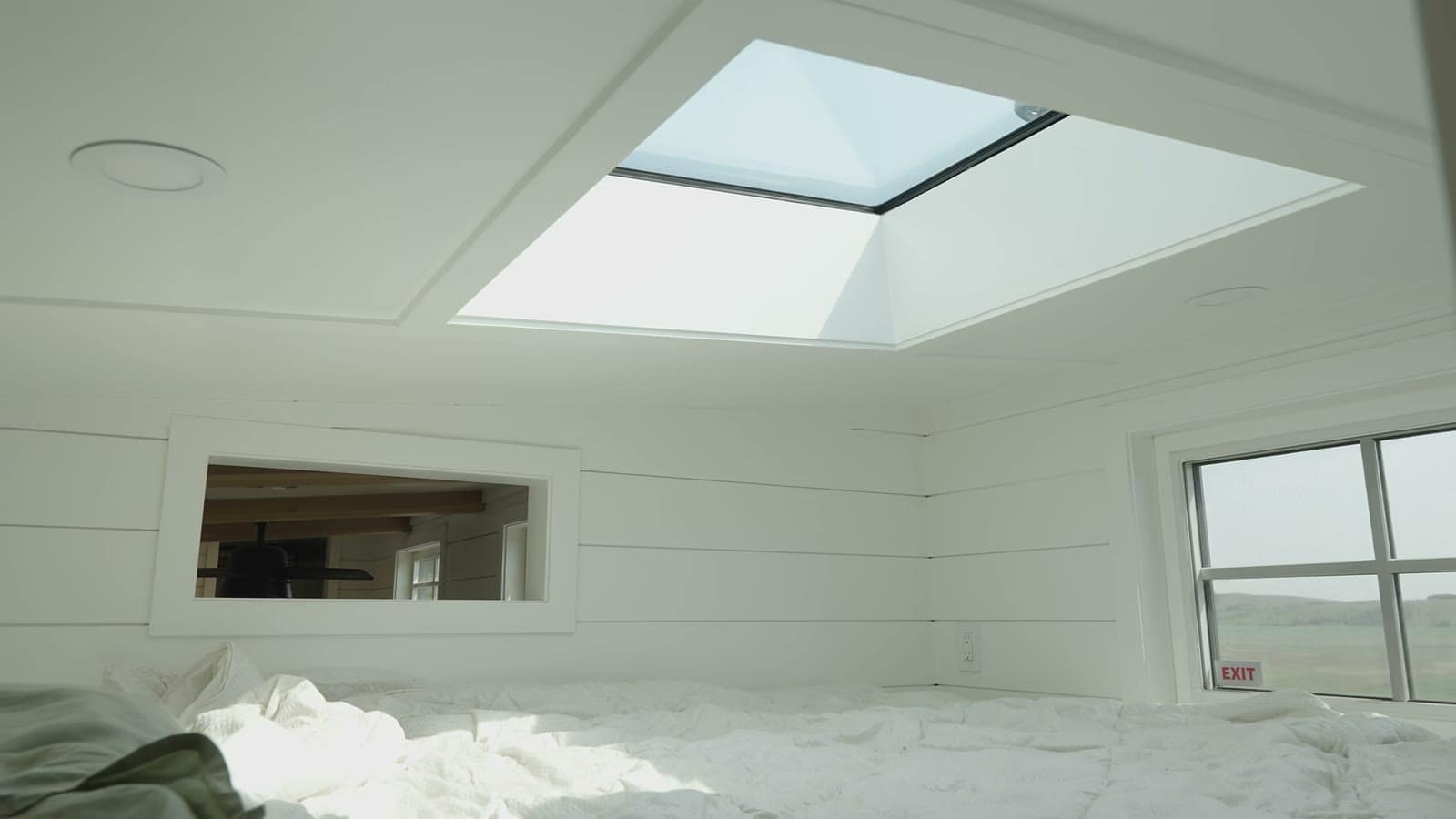 White shiplap sleeping loft with a large skylight and a window looking out over the prairie