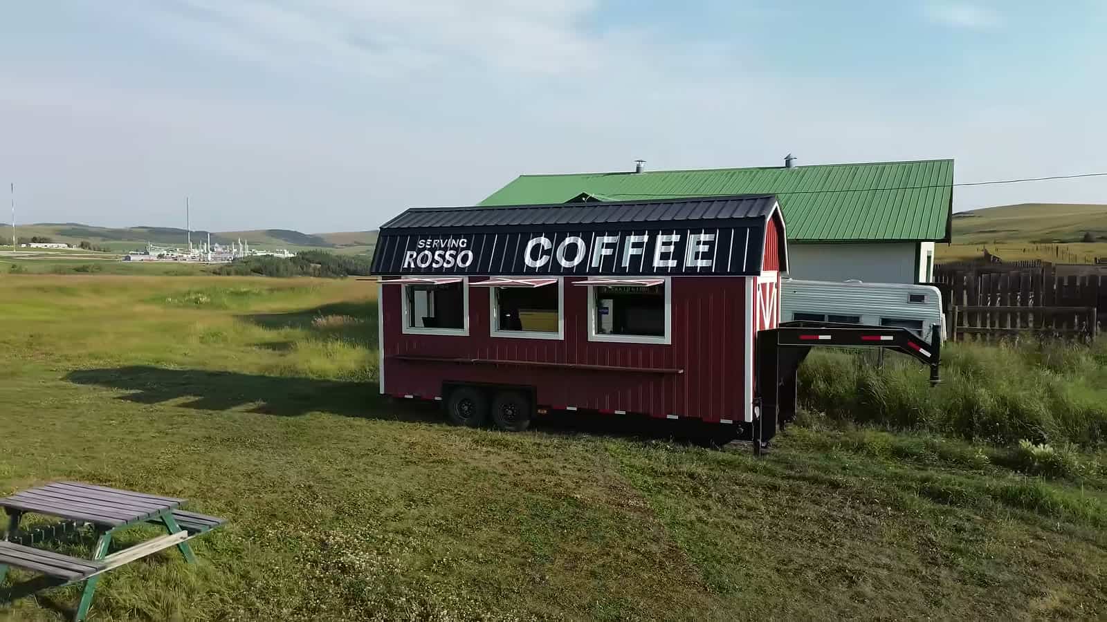 Red barn-style mobile coffee trailer with a black roof sign reading Coffee, parked on the prairie