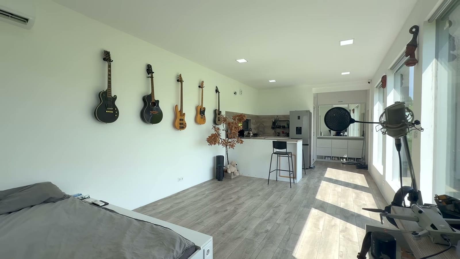 Long open studio with electric and acoustic guitars on the wall, a bed in the foreground, and the kitchen at the far end