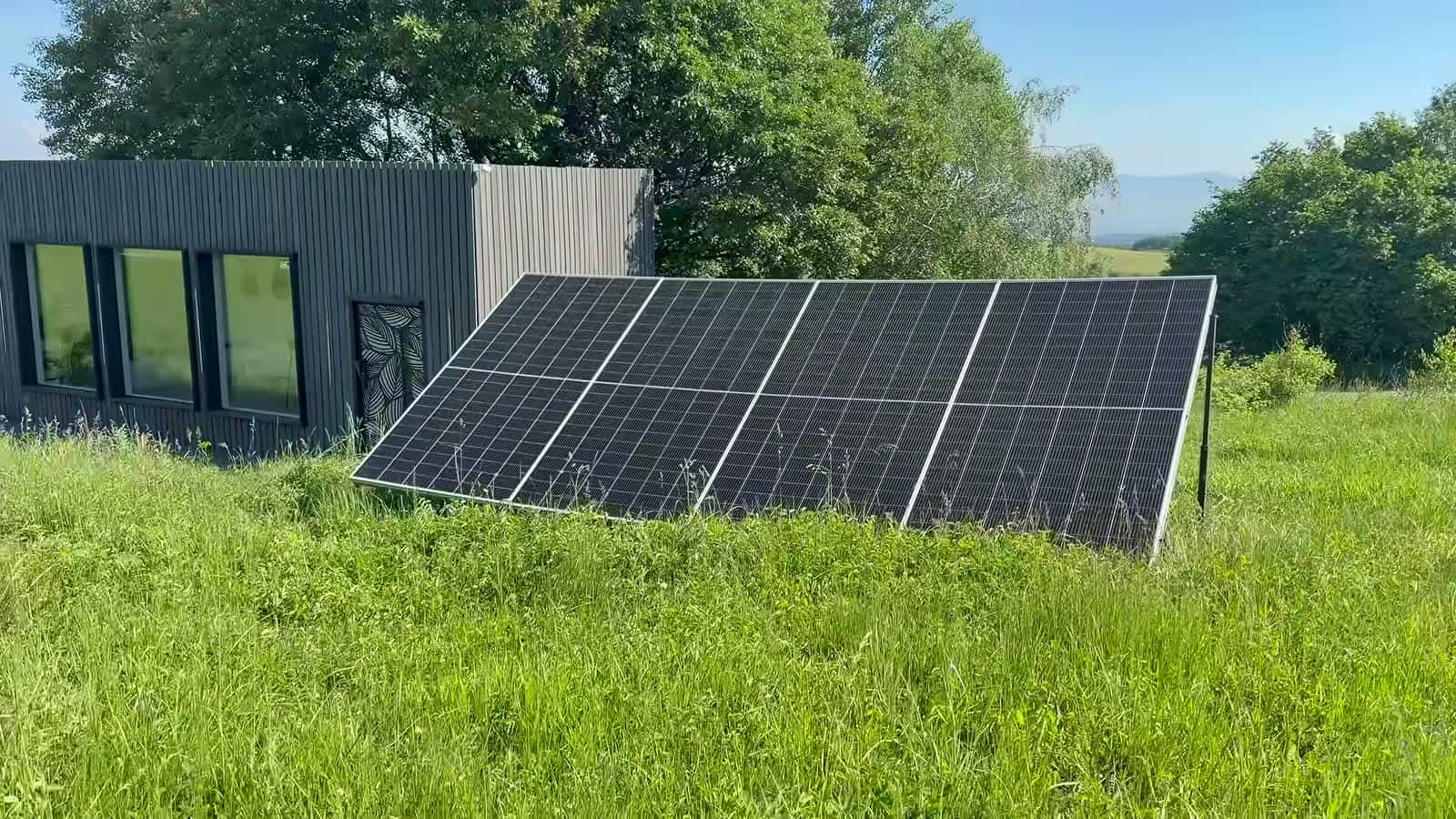 Ground-mounted solar array in tall grass beside the dark-clad studio