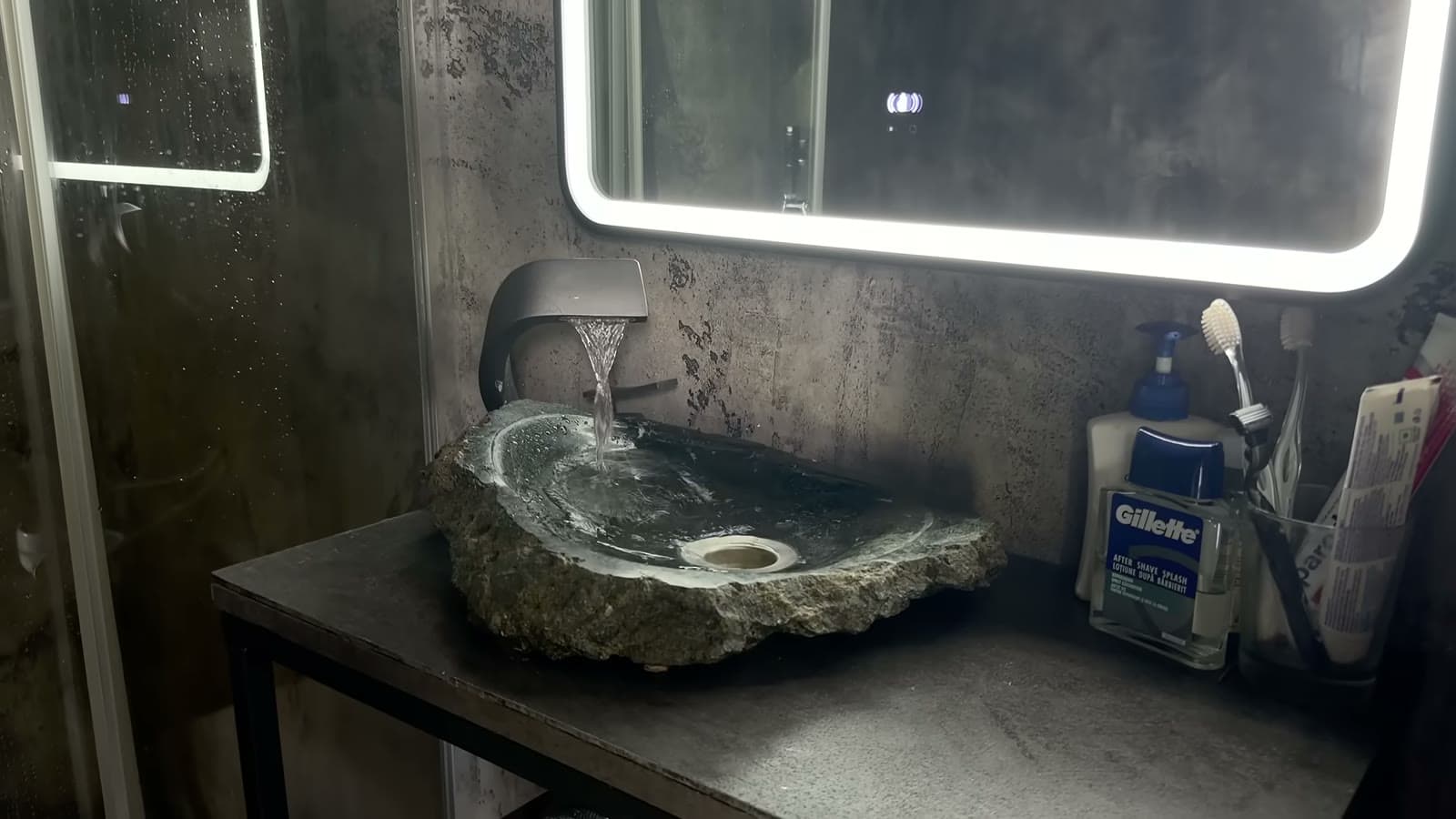 Handmade stone vessel sink under a backlit mirror in the dark bathroom