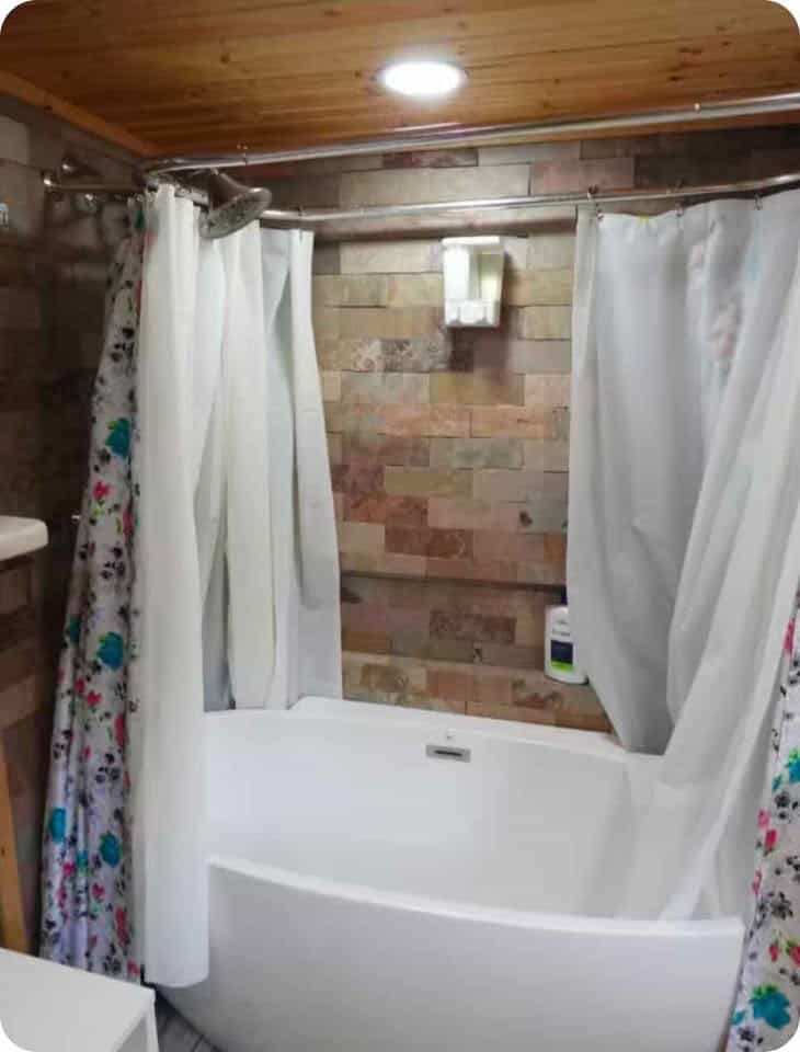 Bathroom with a white soaking tub, stone-look tile wall, and shower curtain