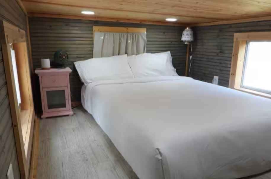 Private bedroom with a white-made bed, wood-paneled walls, and windows on two sides