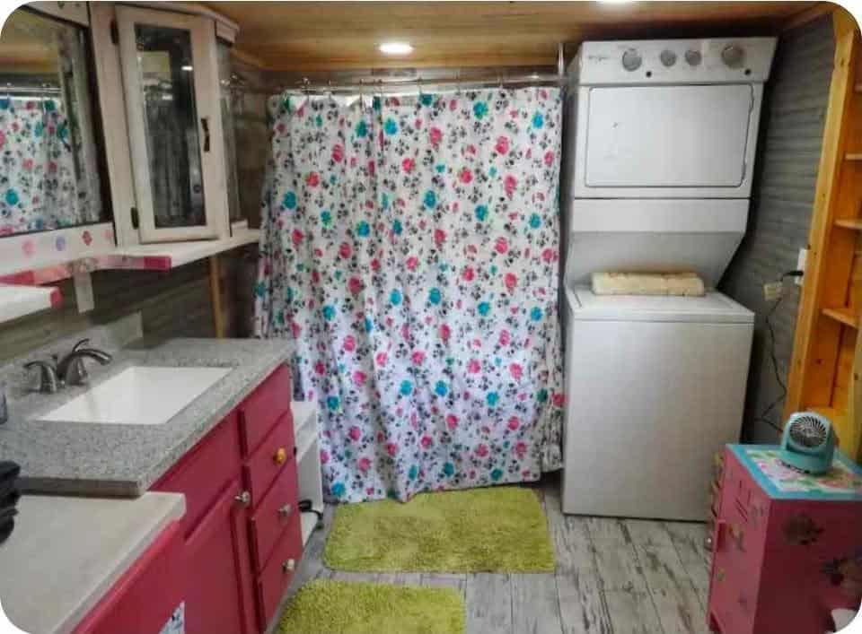 Stacked white washer and dryer next to the vanity and a floral shower curtain
