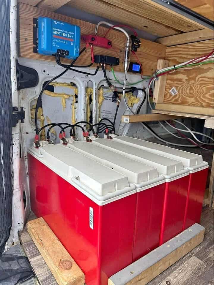 Red battery bank under a Victron solar charge controller and wiring in the rear of the van