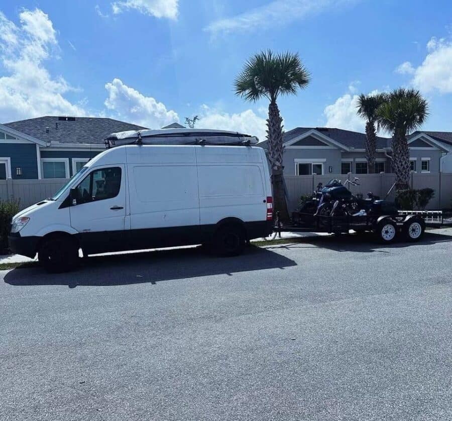 White high-roof Dodge Sprinter camper van with a roof rack parked on a street lined with palm trees