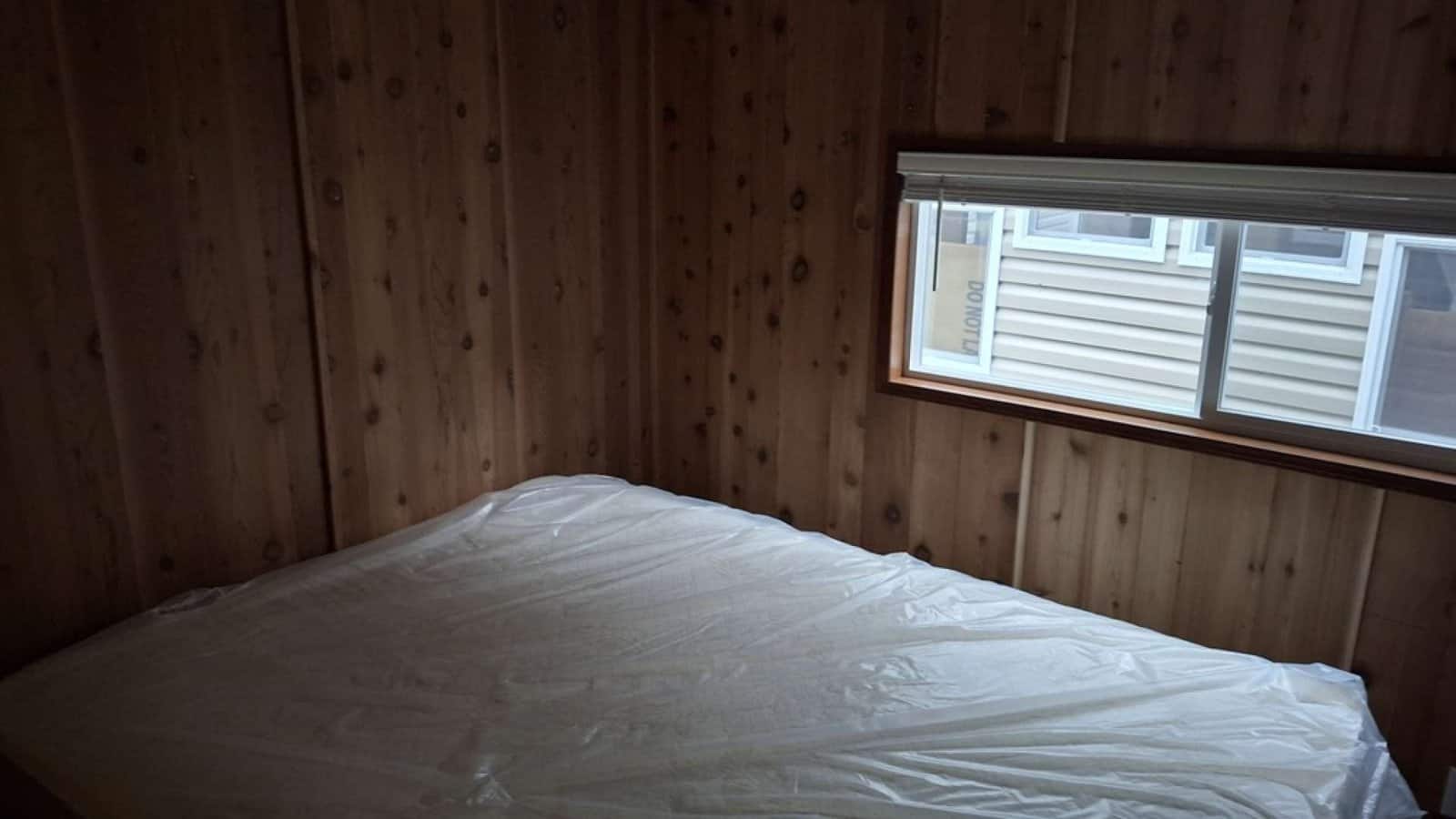Ground-floor bedroom with dark wood paneling, a queen mattress, and a side window