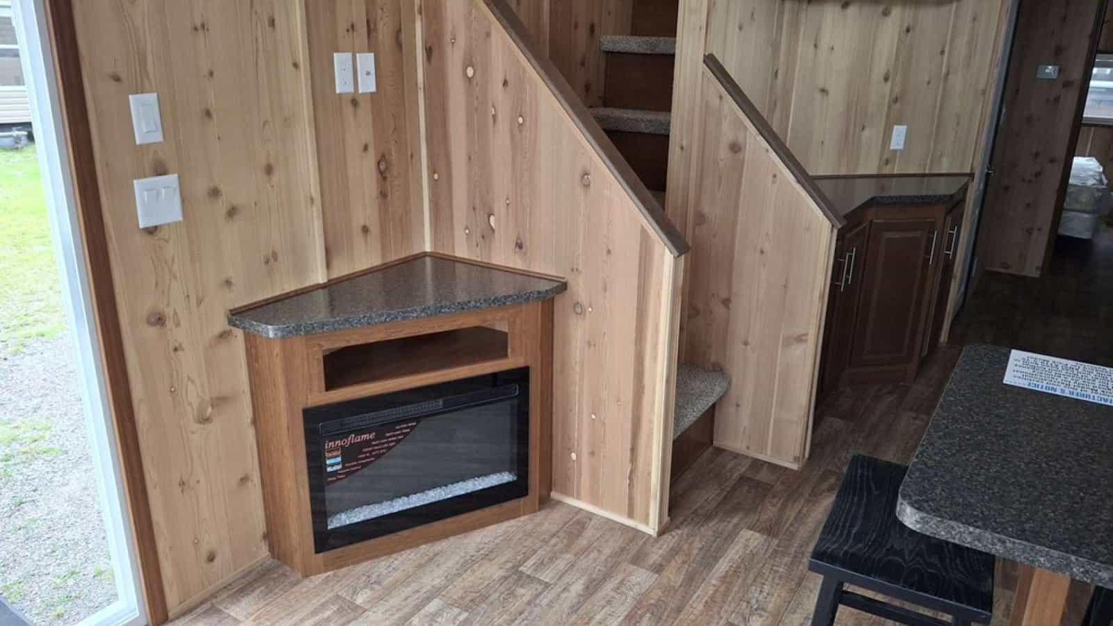 Electric fireplace in a wood surround beside the cedar-paneled stairs to the loft