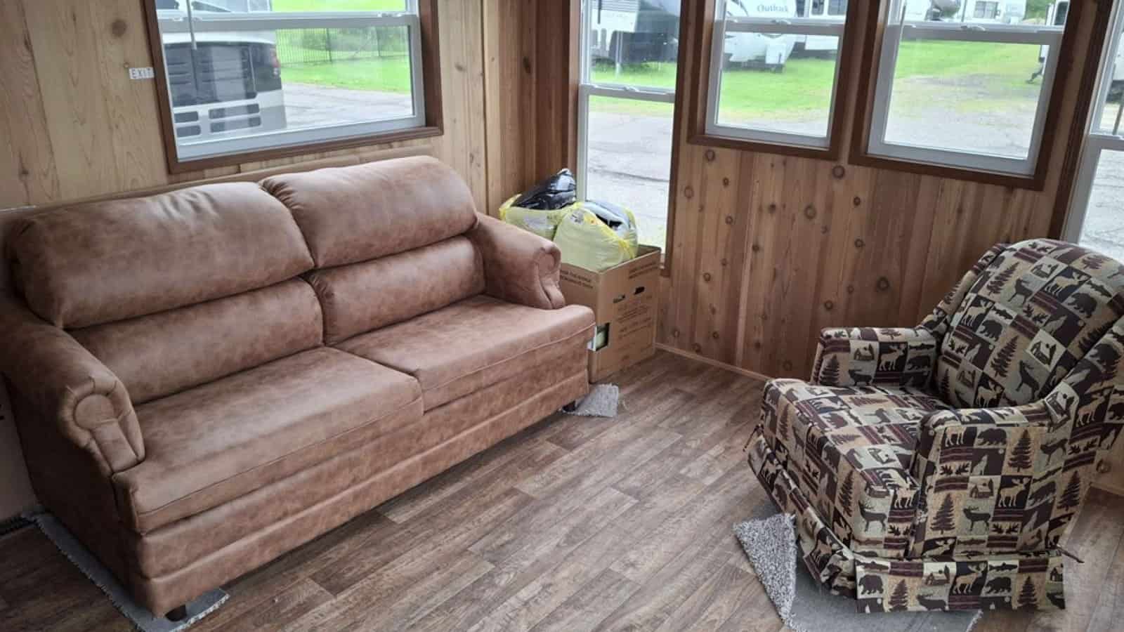 Living room with cedar-paneled walls, a tan sofa, a patterned recliner, and windows