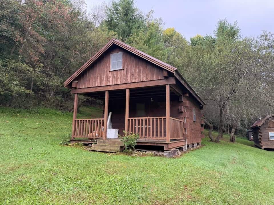 Front of the log cabin with a covered porch, railings, and wooden steps